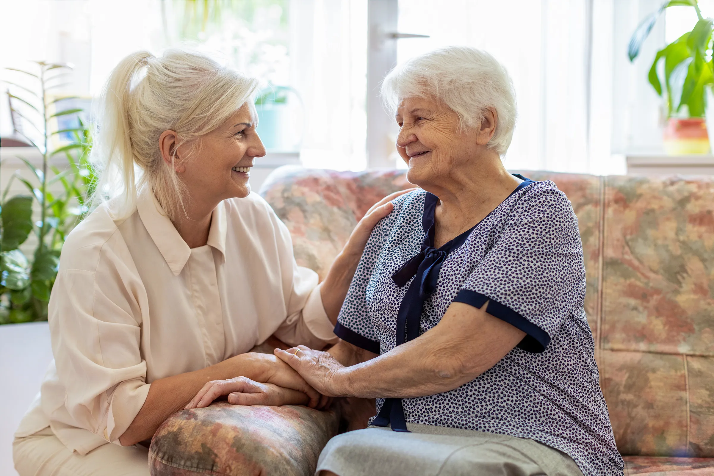Caregiver and elderly woman holding hands on couch
