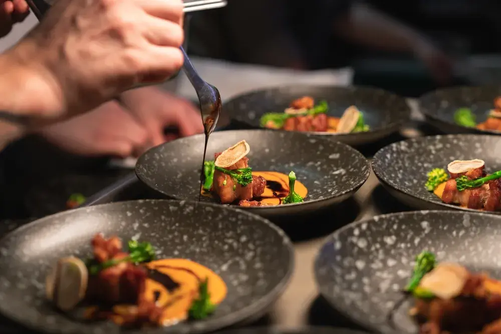 Chef drizzles sauce over plated gourmet meat dishes