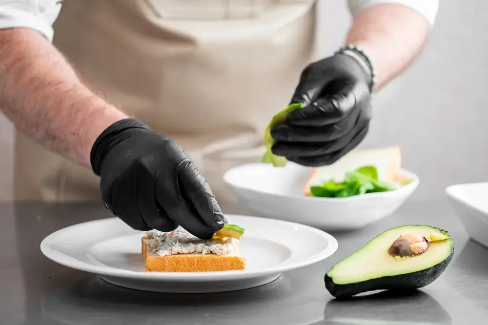 Chef garnishing open-faced sandwich beside halved avocado
