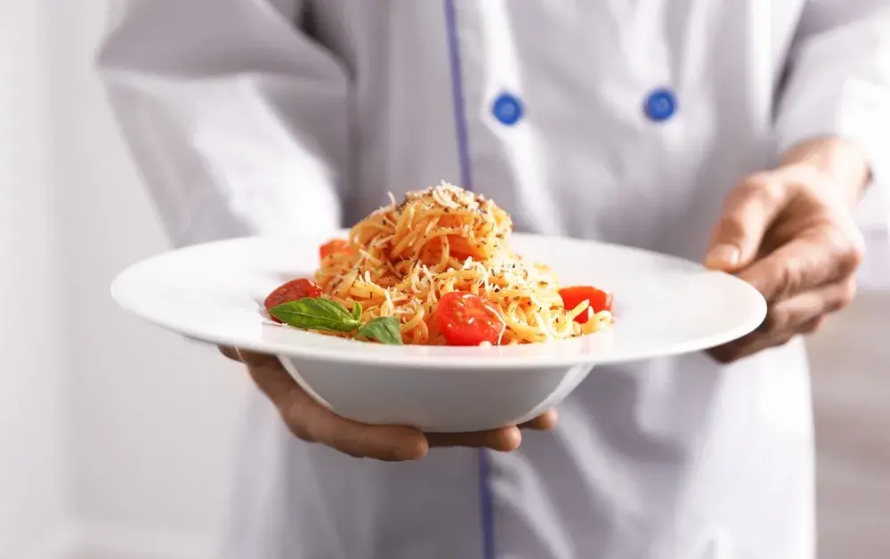 Chef holding spaghetti with tomatoes, basil, and grated cheese